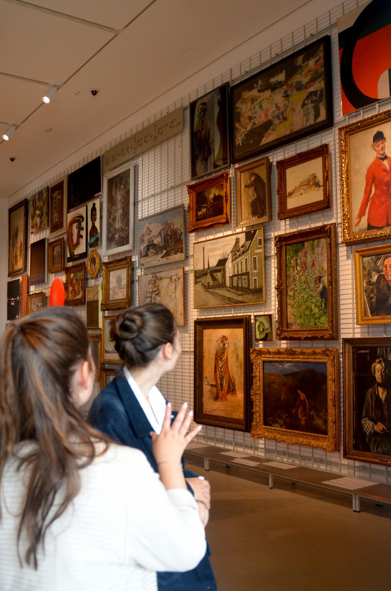 zwei Frauen betrachten eine Bilderwand in einer Galerie